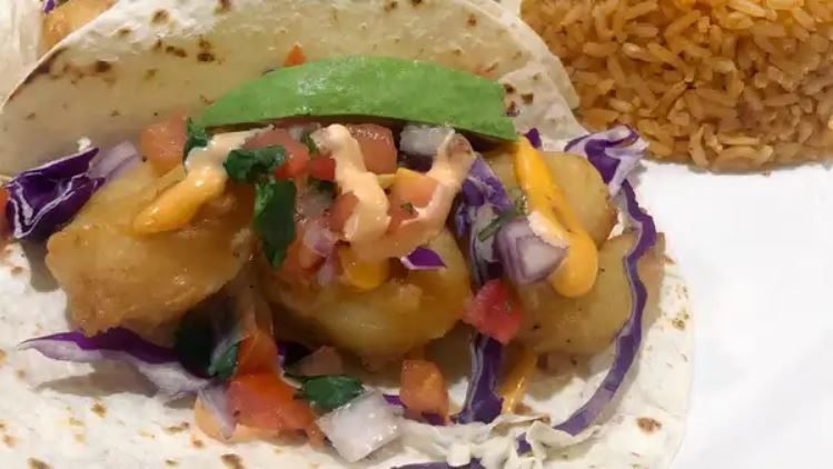 A beer battered shrimp taco with red cabbage, pico de gallo, chipotle sauce and avocado, beside Mexican rice.