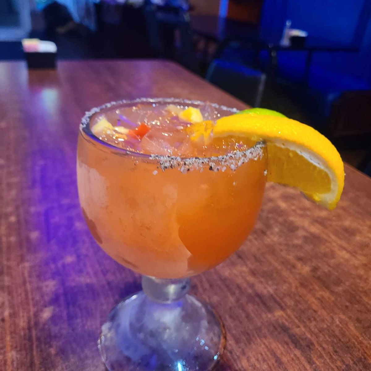 A salt-rimmed margarita on a wood table in the La Costa dining room, the blue vinyl booths and purple lights behind it.