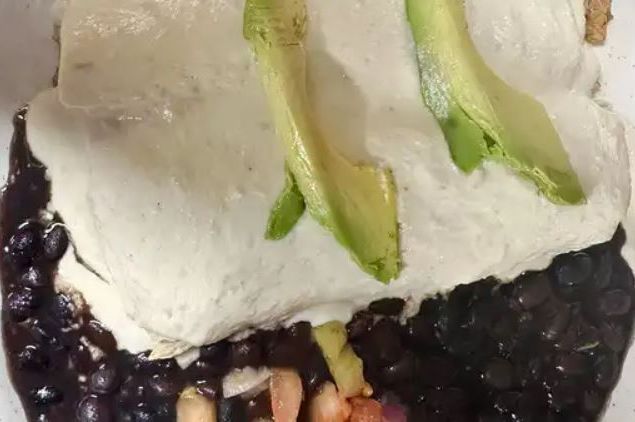 Angel's Enchilada under the green tomatillo cream cheese sauce, sliced avocado on top, black beans around the plate.